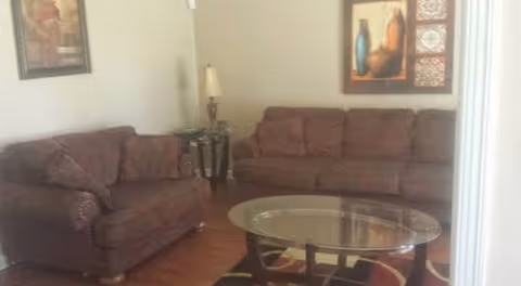 Living room with brown couches, glass coffee table, lamp, and wall art.