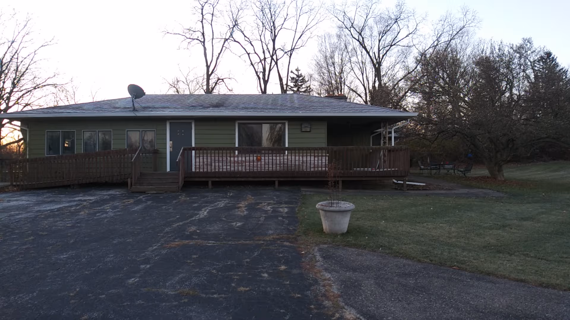Front view of a single-story green building with a wooden deck and driveway.