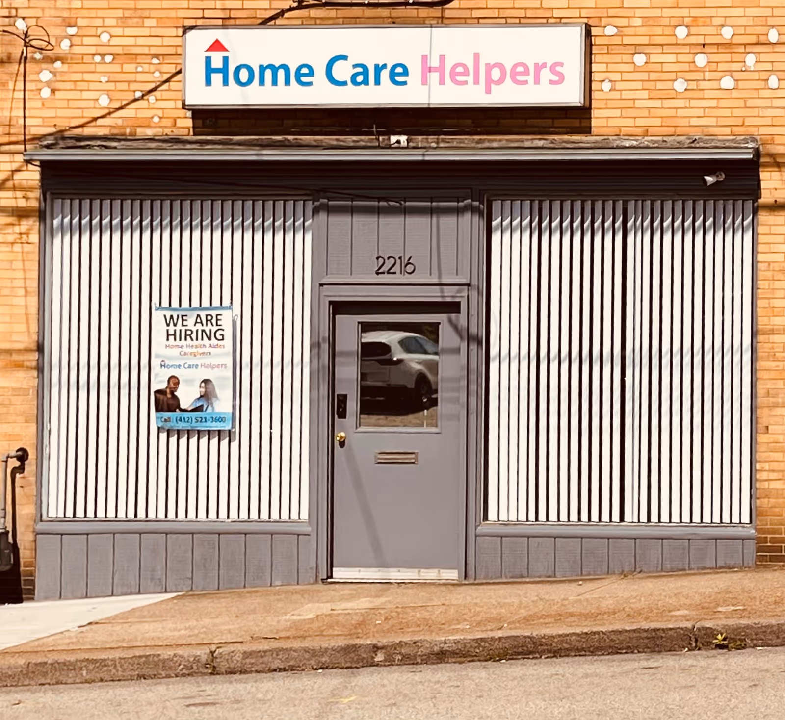 Exterior storefront of Home Care Helpers LLC with a central door and hiring poster.