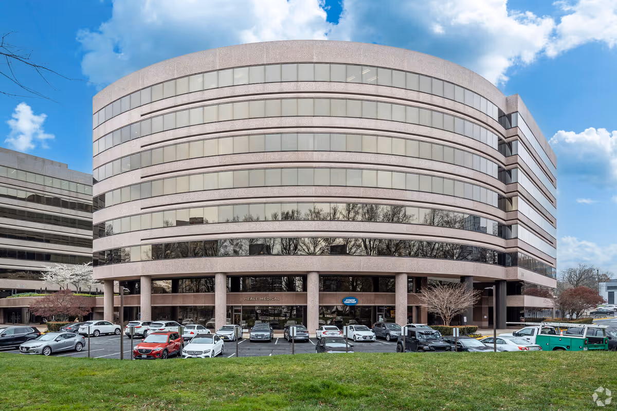 Curved modern office building with glass windows and a front parking lot.