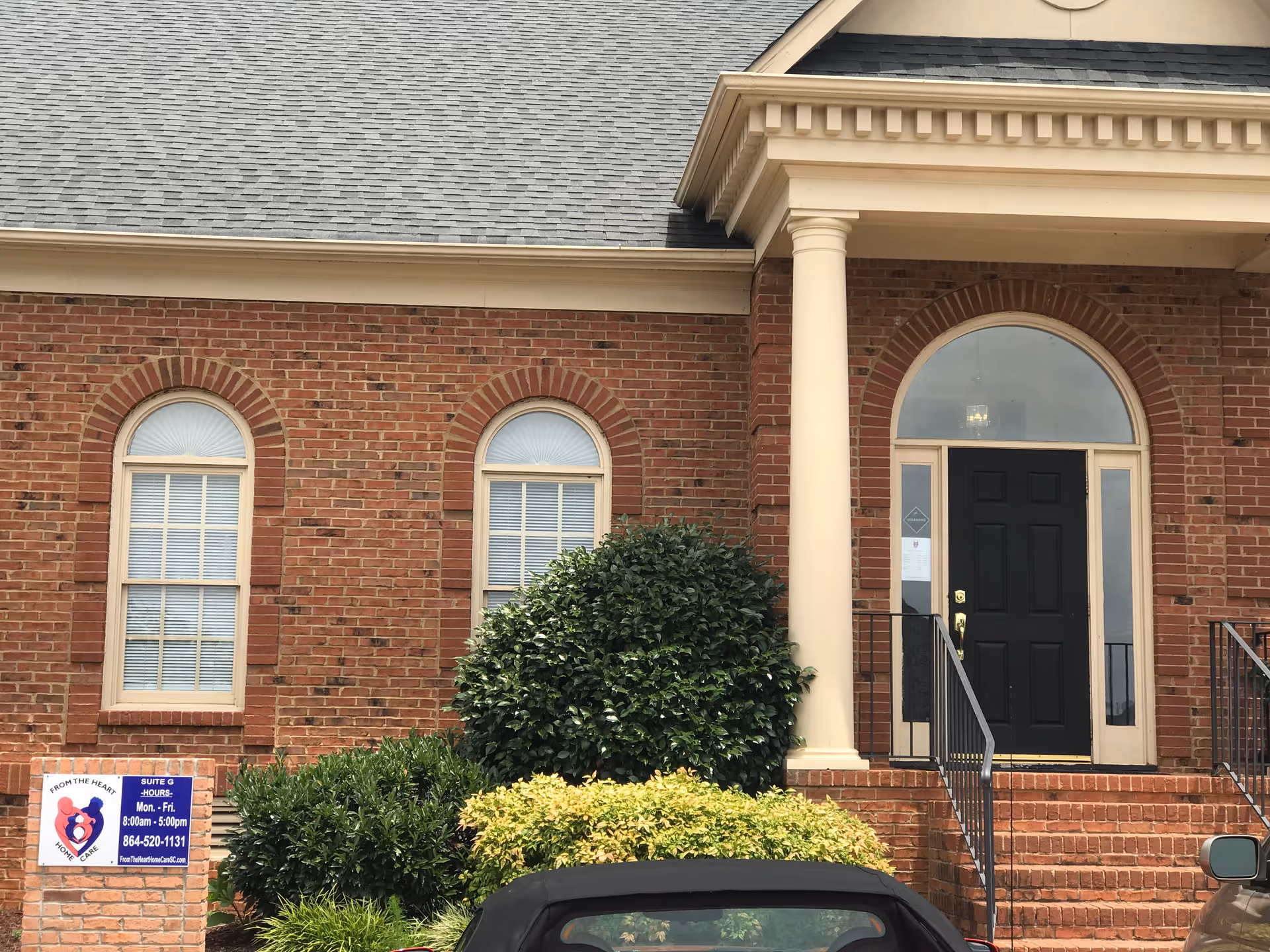 Brick building exterior with arched windows, columns, and a dark front door.