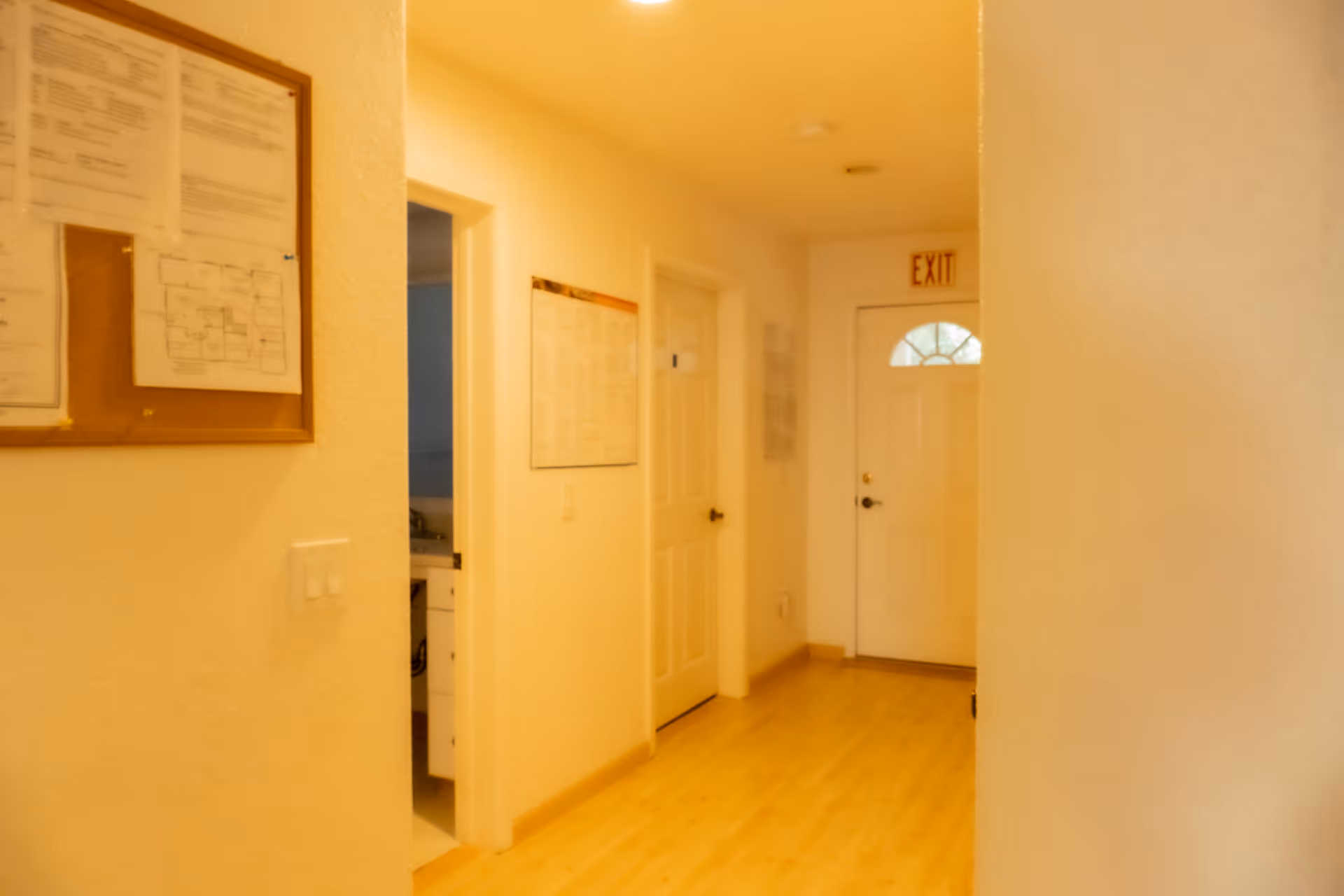 Hallway in a senior living facility with doors, bulletin boards, and an exit sign.