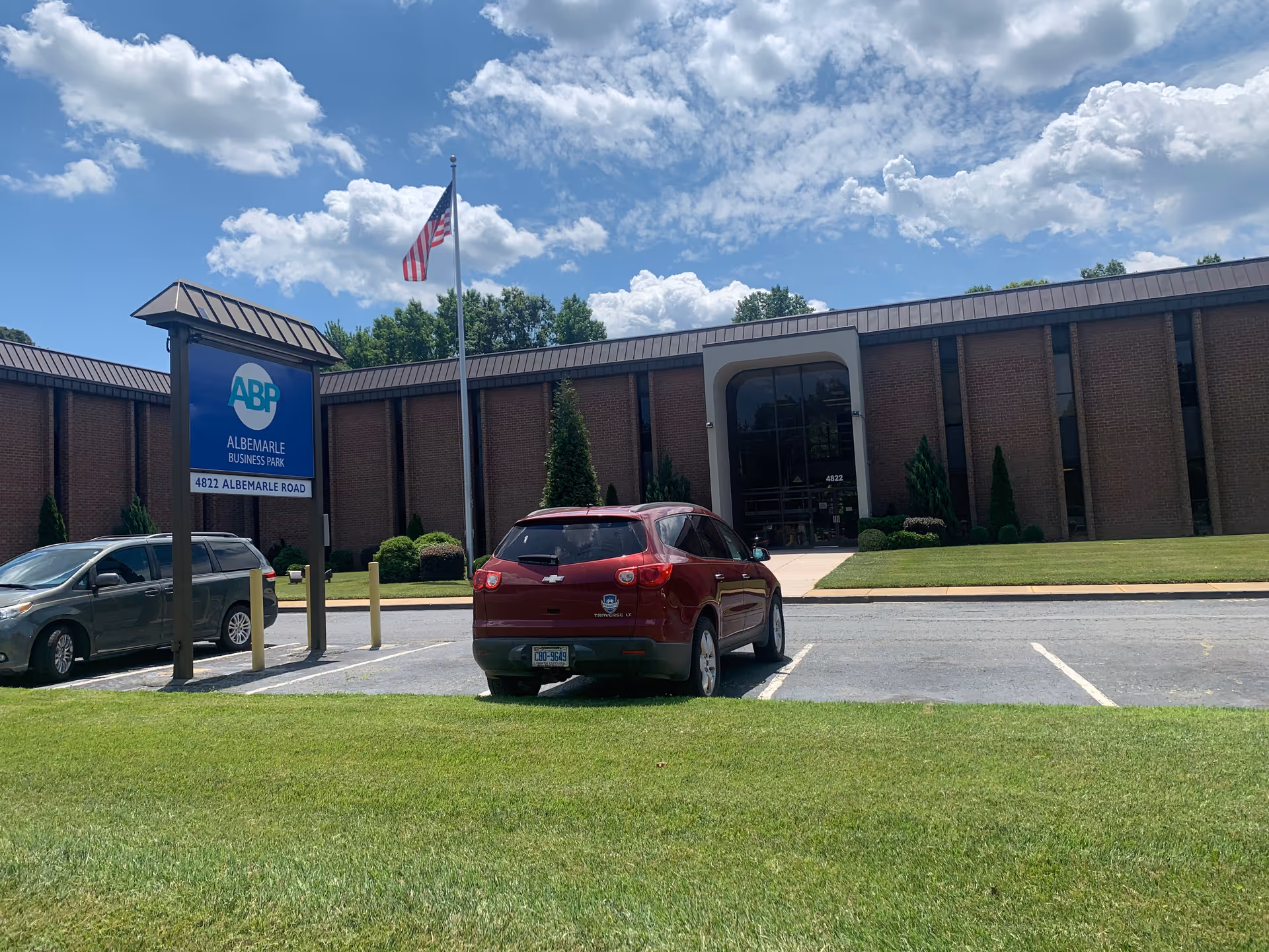 Exterior view of a brick building with a parking lot and American flag.