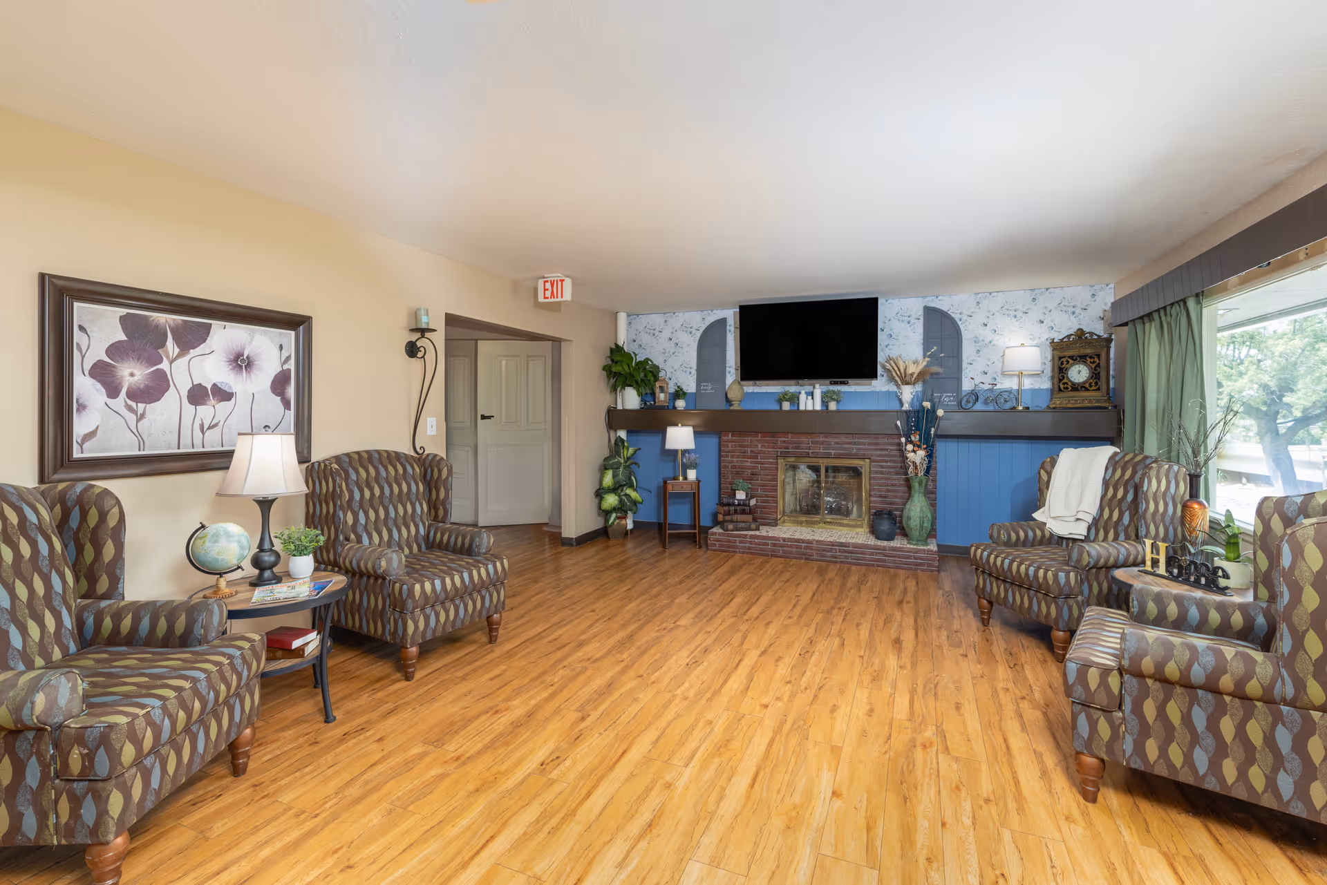 Cozy senior living room with patterned chairs, a brick fireplace, and a mounted TV.
