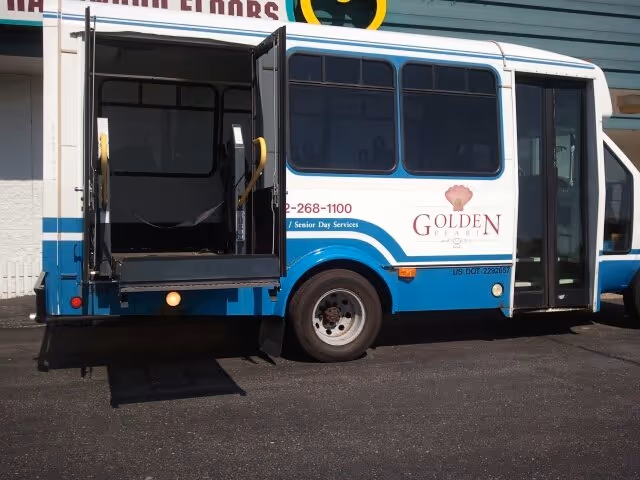 Blue and white shuttle bus with lowered ramp parked outside Oakmont of the Terraces.