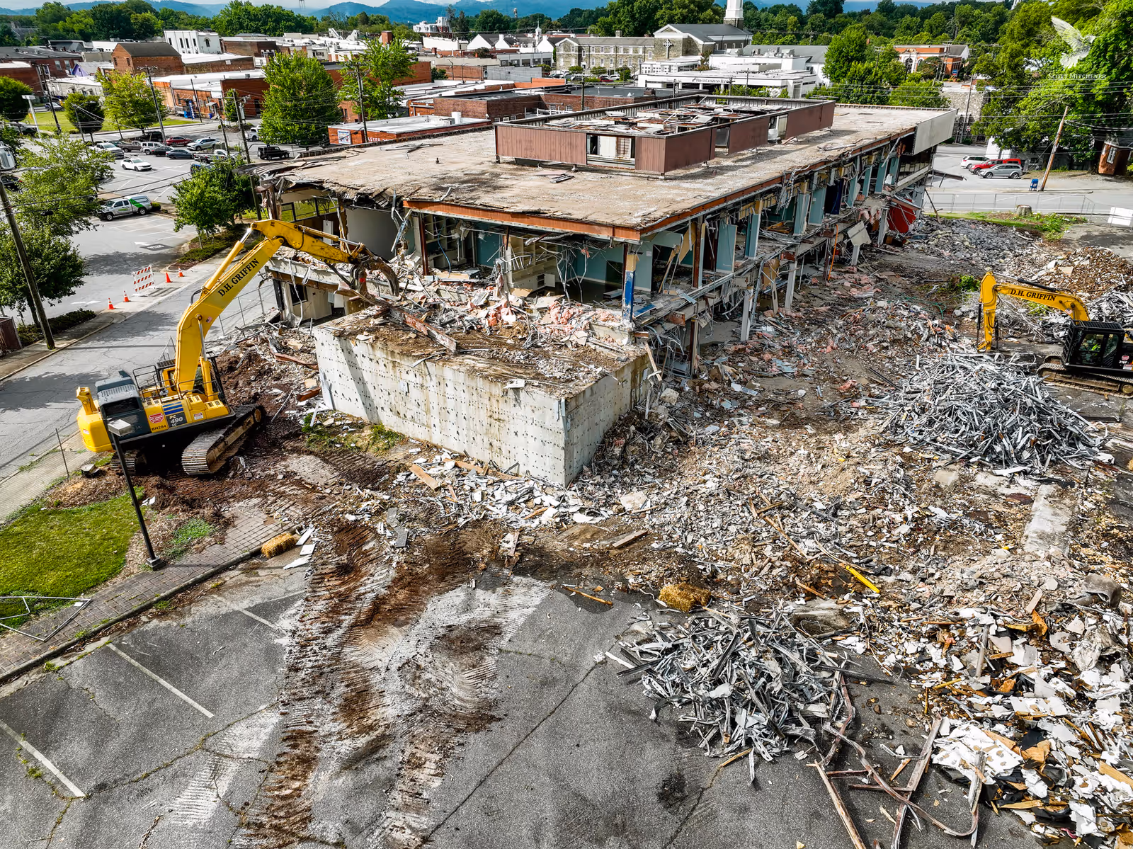 Partially demolished two-story building with piles of debris and two excavators.