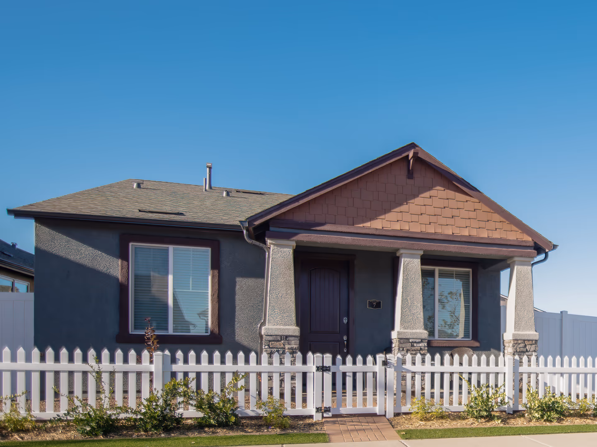 Single-story house with a white picket fence and front garden under clear blue sky.
