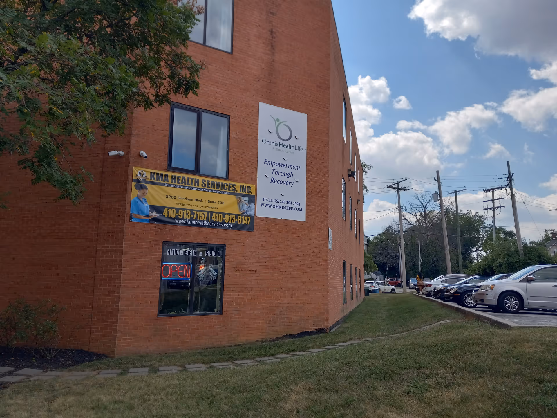 Brick building exterior with KMA Health Services banners and a row of parked cars.