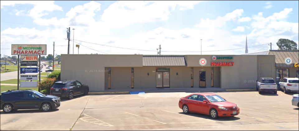Exterior of a strip mall with a pharmacy sign and parked cars.