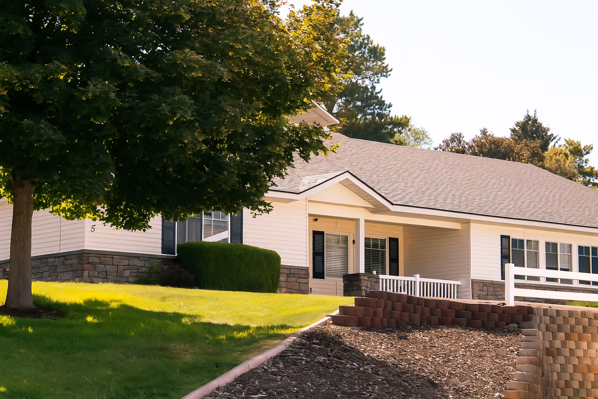 Front exterior of a single-story memory care facility with white siding and stone accents.