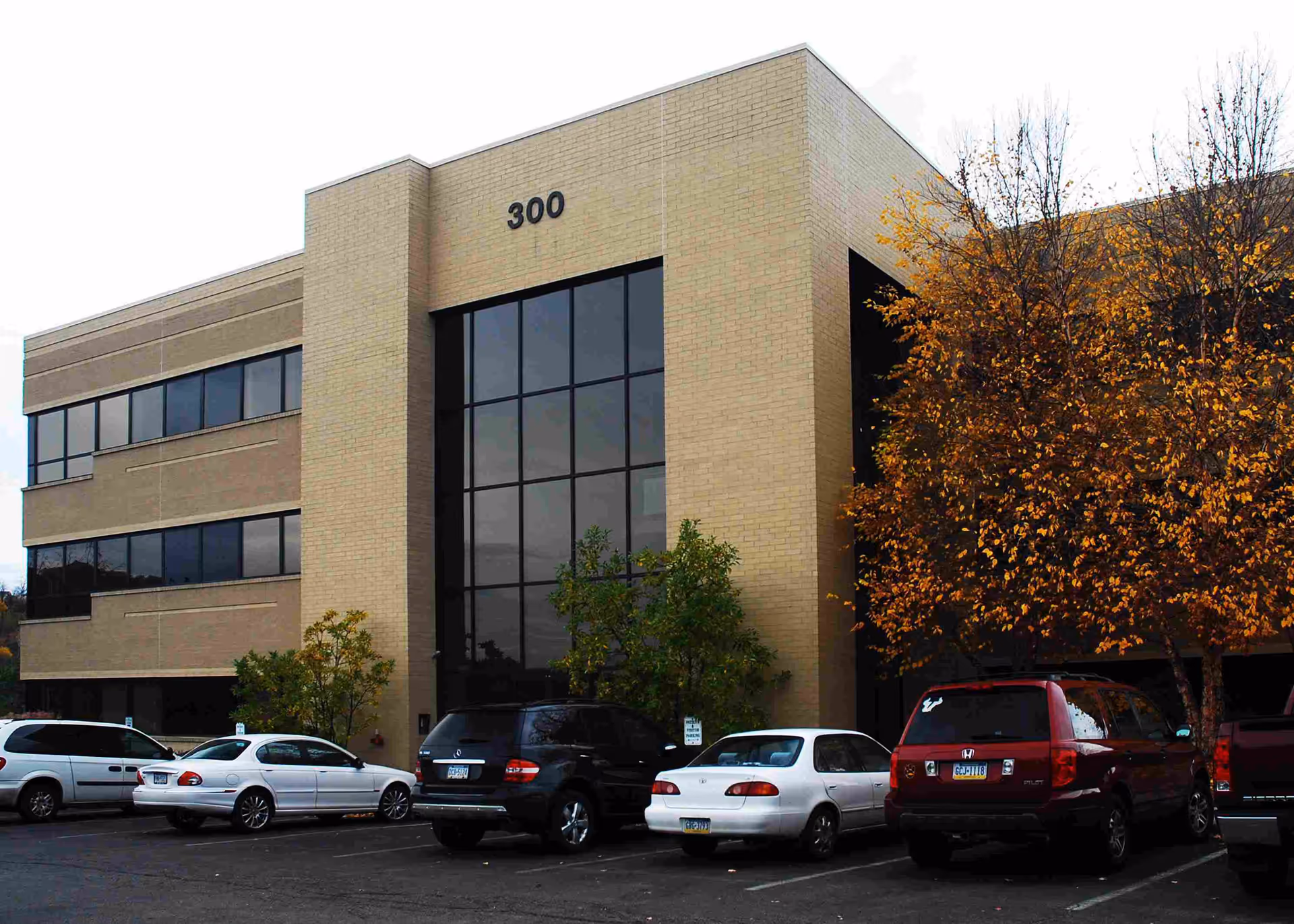 Front view of a brick building with a large glass entrance and parked cars.