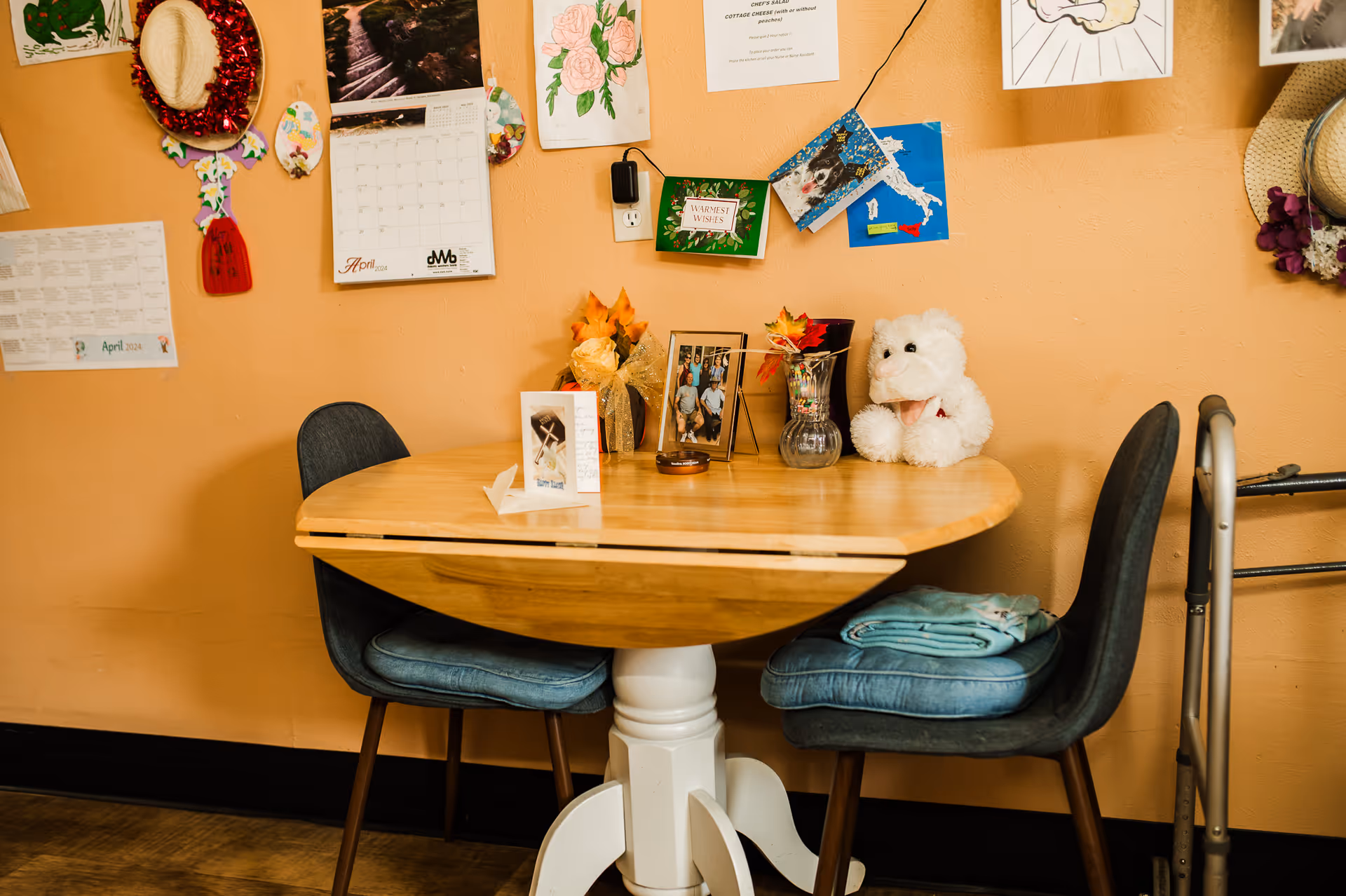 Round wooden table with two teal chairs in a dining area, teddy bear and wall decorations.