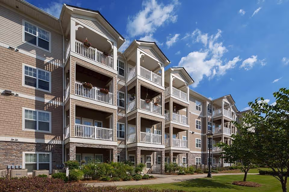 Multi-story senior living building with balconies and landscaped courtyard under blue sky