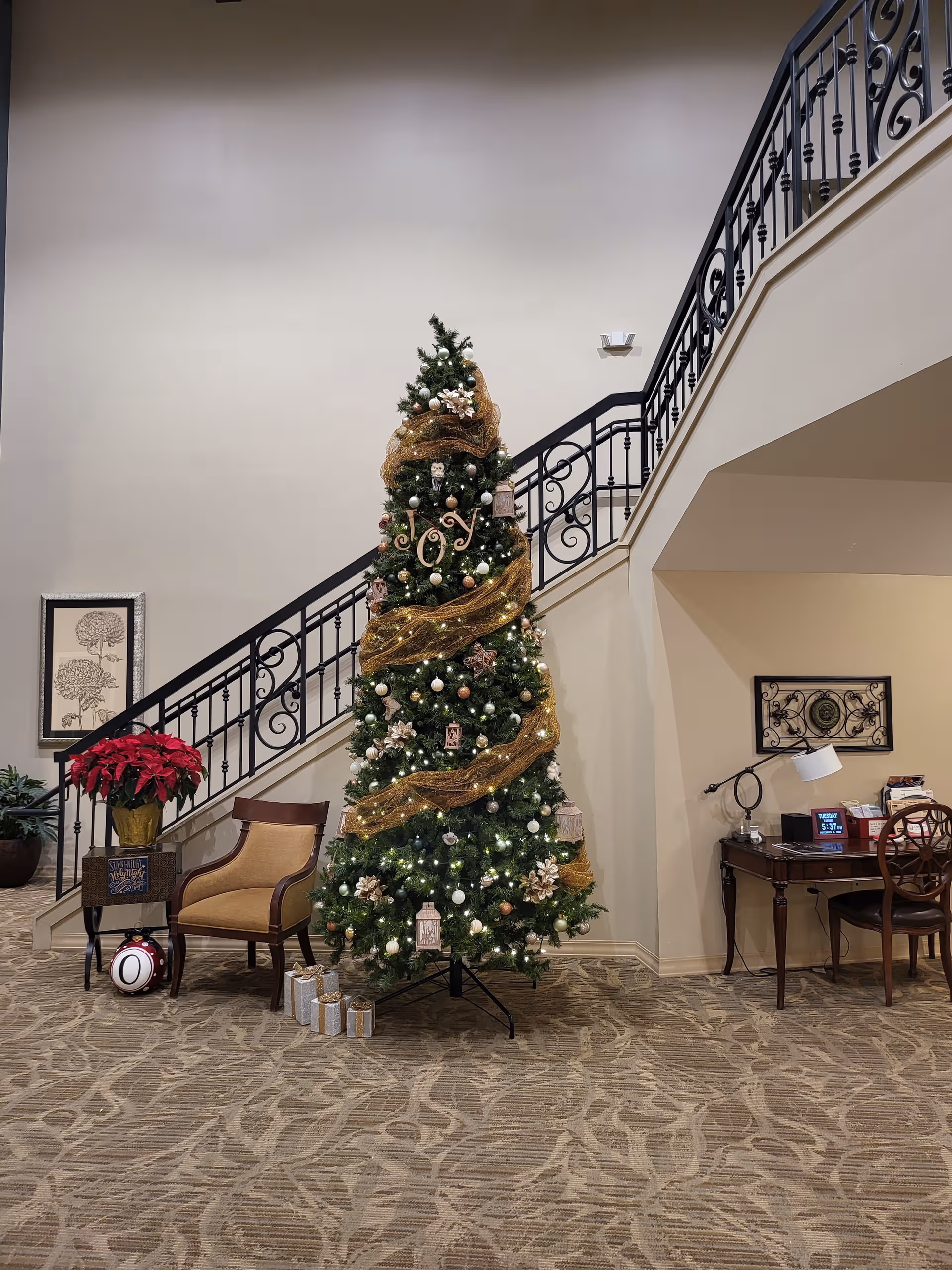 Interior lobby with a tall Christmas tree, wrapped garland, and a curved staircase.