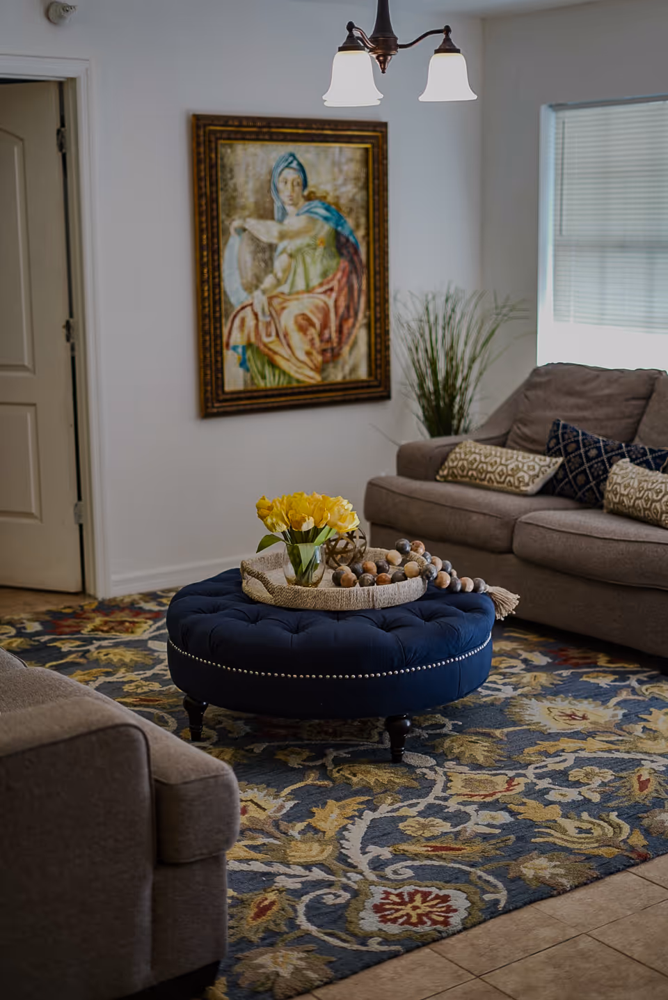 Cozy living room with gray sofa, blue tufted ottoman, and wall art.