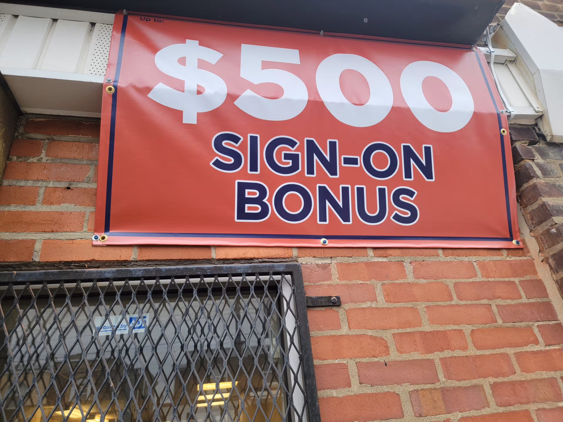 Red banner advertising a $500 sign-on bonus mounted on a brick building exterior