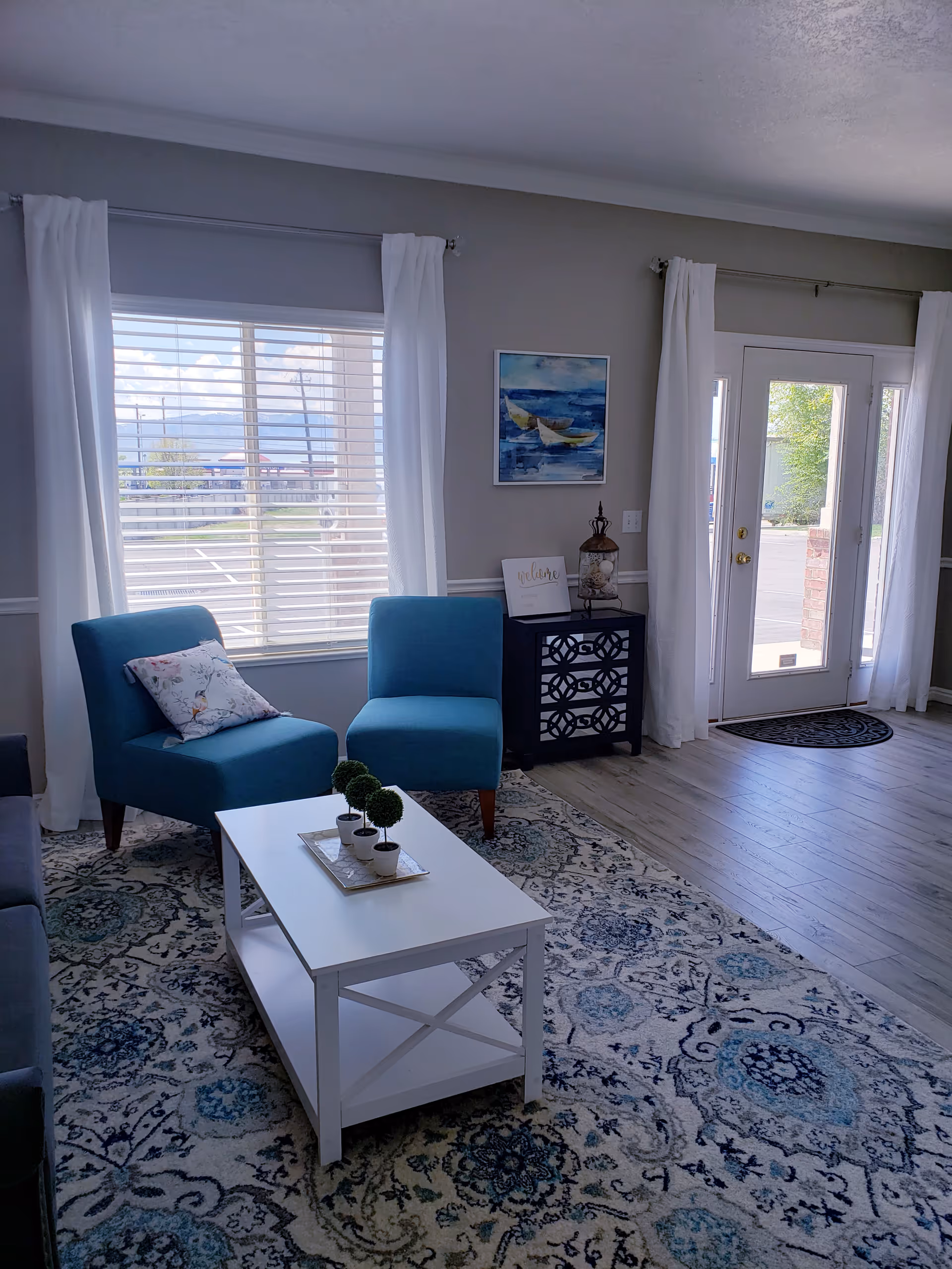 Bright living room with blue chairs, white coffee table, and large windows.