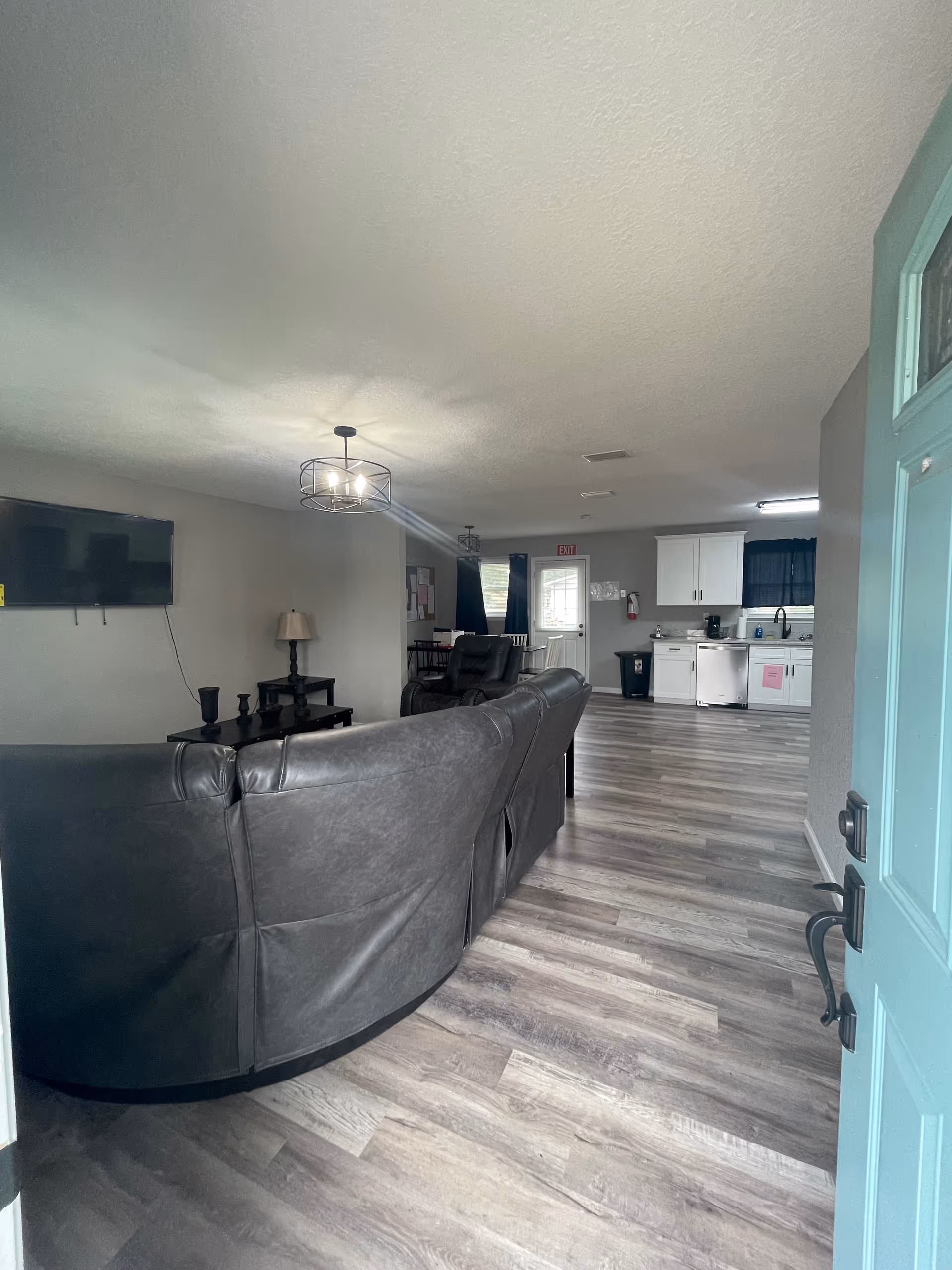Open-concept living room with a curved sectional, TV, and nearby kitchen.