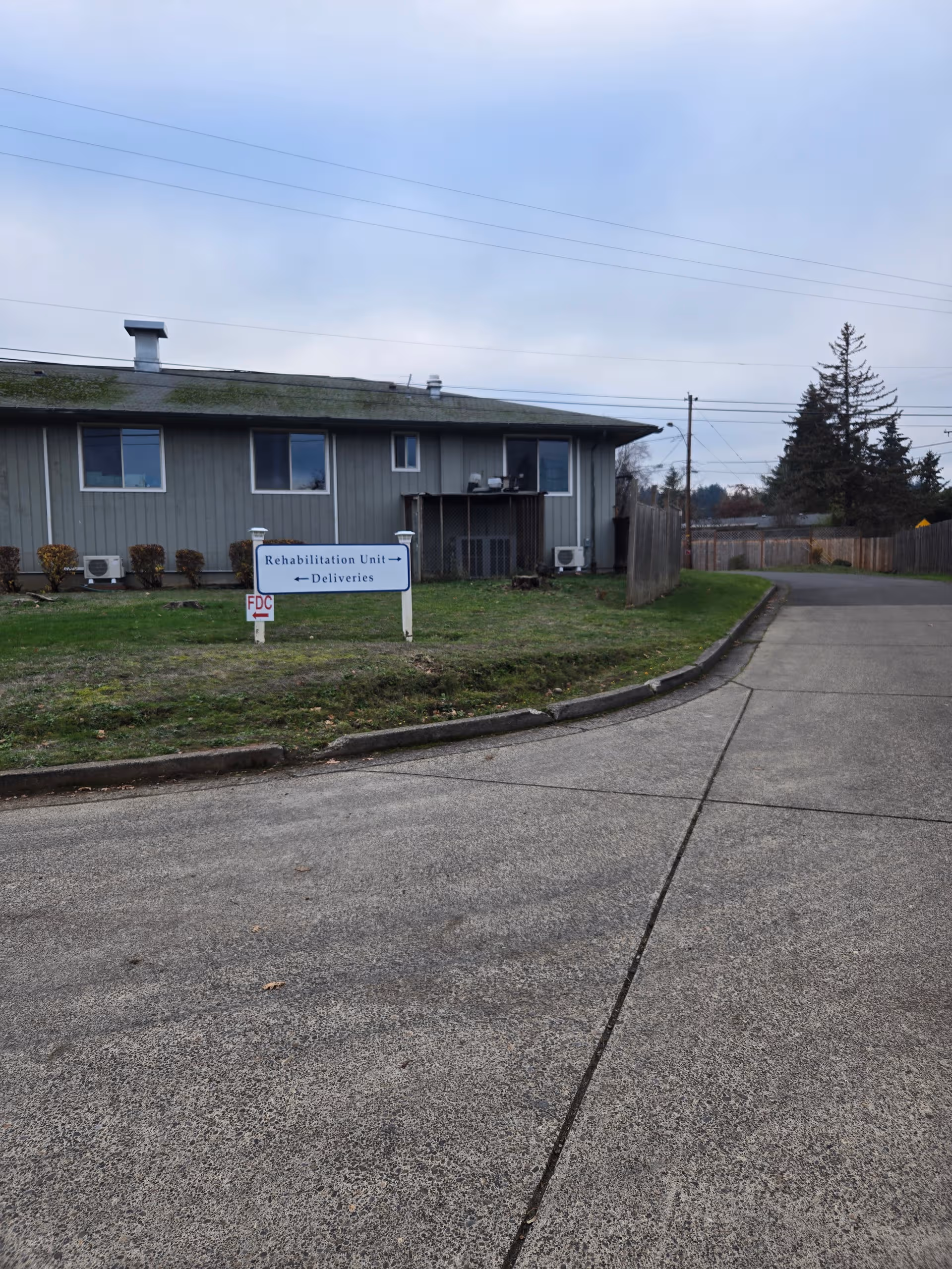 Single-story rehabilitation facility exterior with a deliveries sign beside a curved driveway.