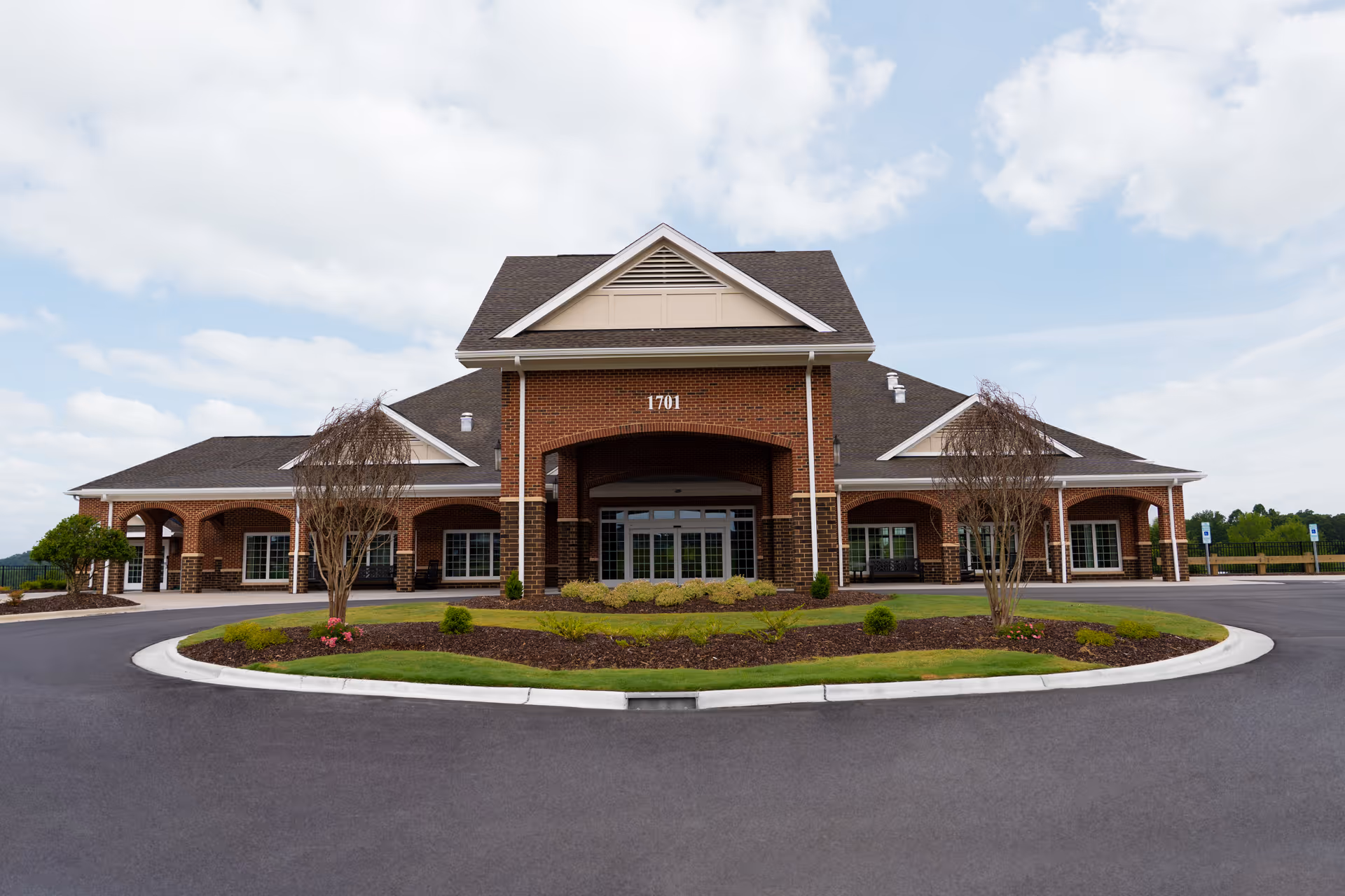 Front exterior of a brick senior living facility with a covered main entrance, porticos, and a circular driveway.