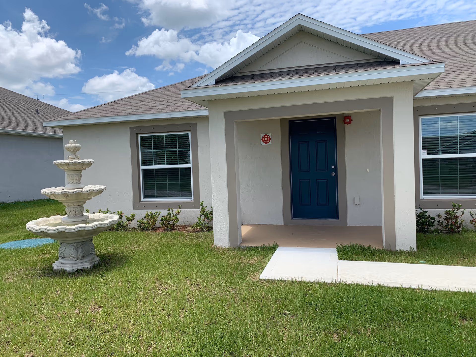 Front exterior of Compassion Homecare System LLC, showing the blue door, porch, lawn, and fountain.