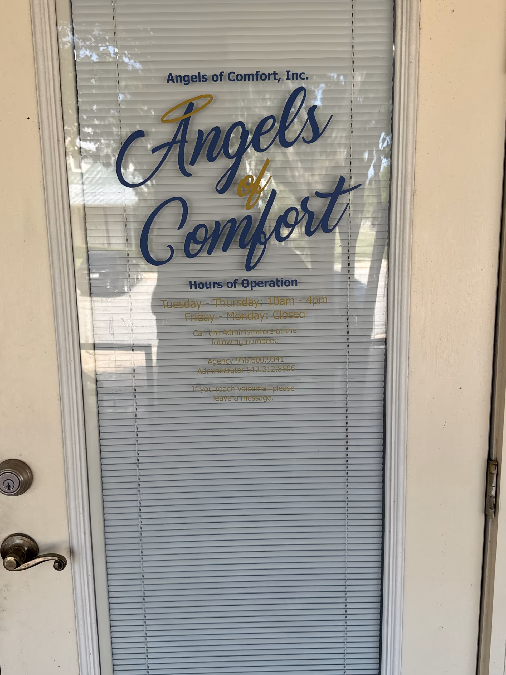 Glass door with blinds displaying Angels of Comfort sign and hours.