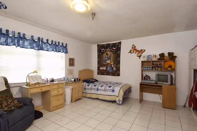 Bedroom in a senior living facility featuring a bed, desk, sofa, and TV.