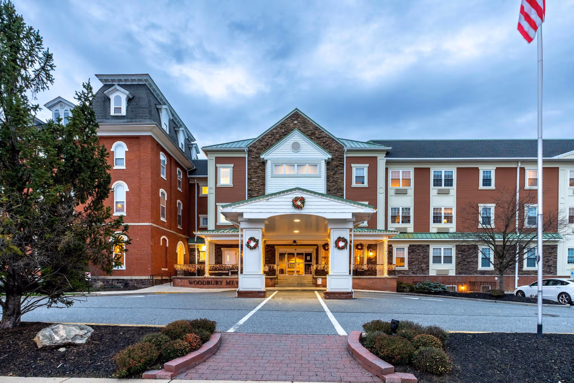 Exterior view of Woodbury Mews senior living facility with a covered entrance and holiday wreaths.