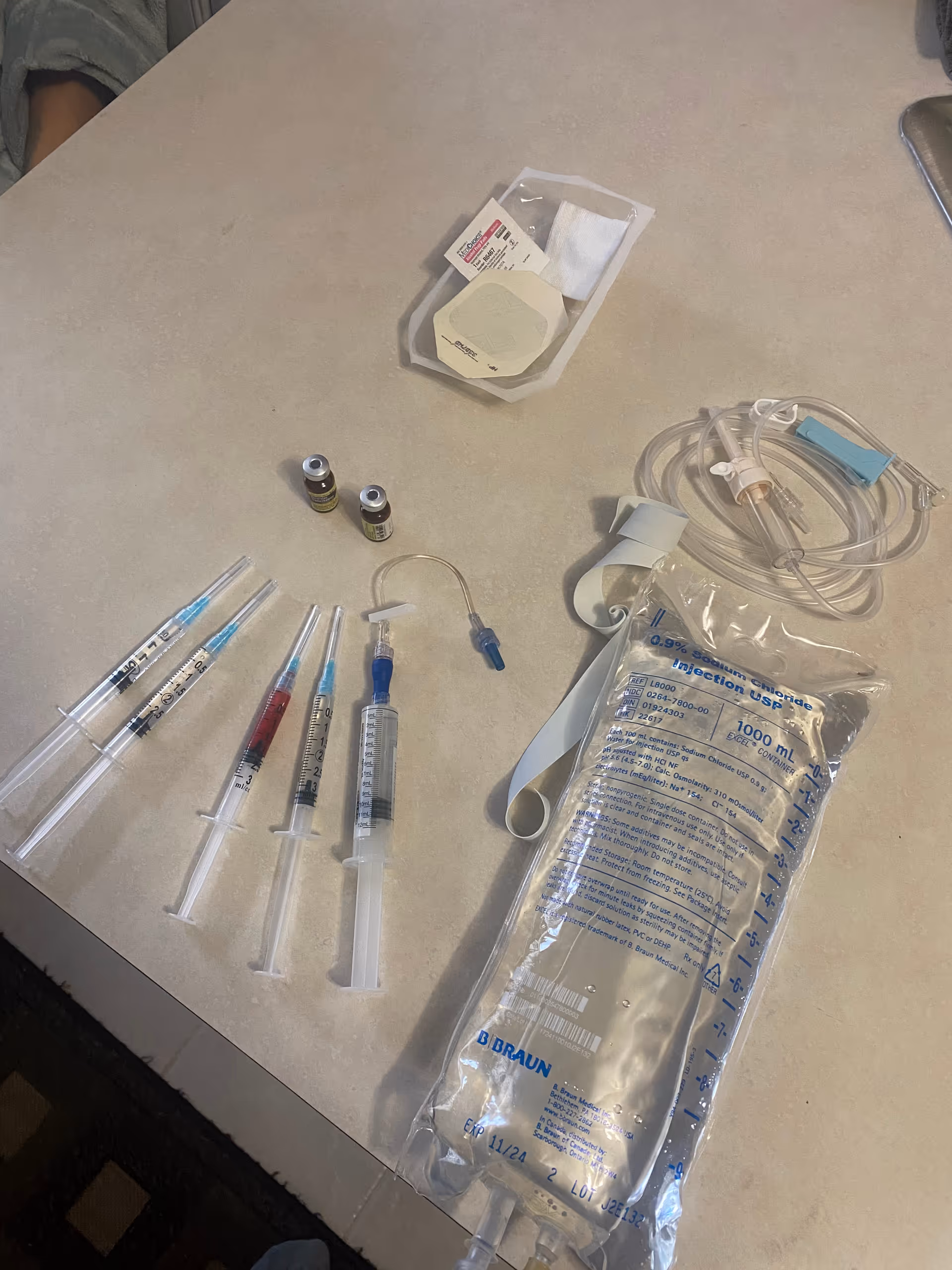 Medical infusion supplies including syringes, vials, and an IV bag on a table.