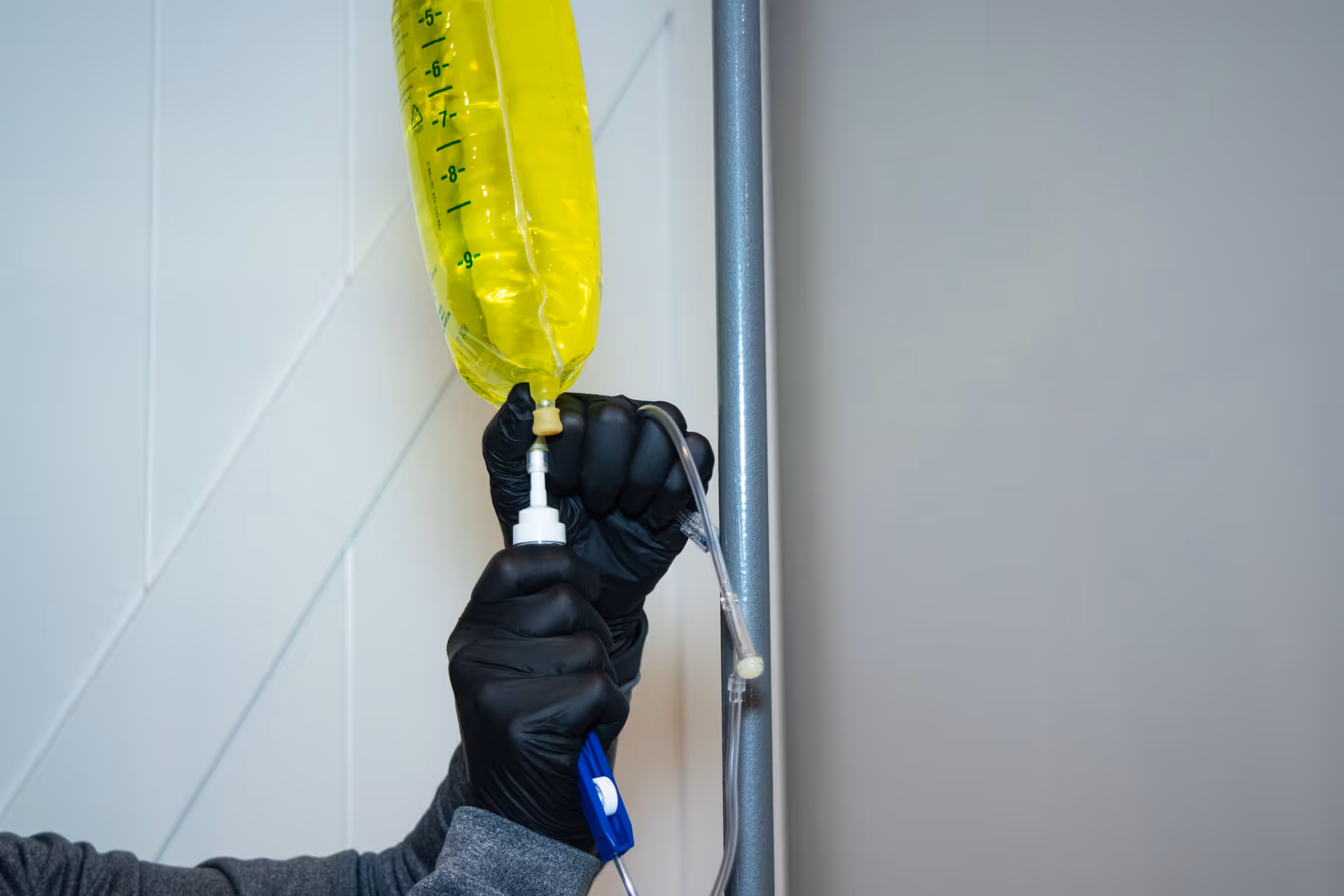 Close-up of gloved hands attaching an IV bag to a metal IV pole.