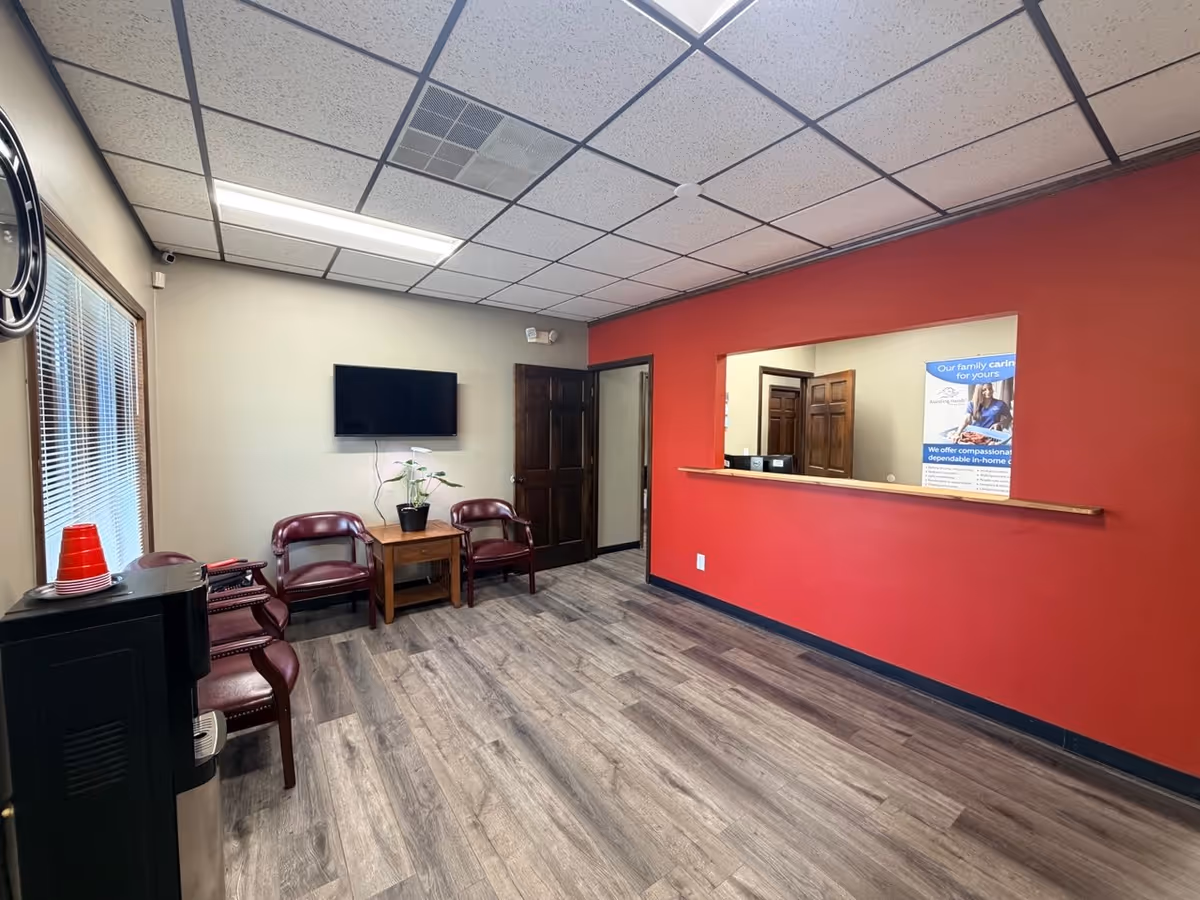 Waiting area with red accent wall, chairs, plant, and a pass-through window.