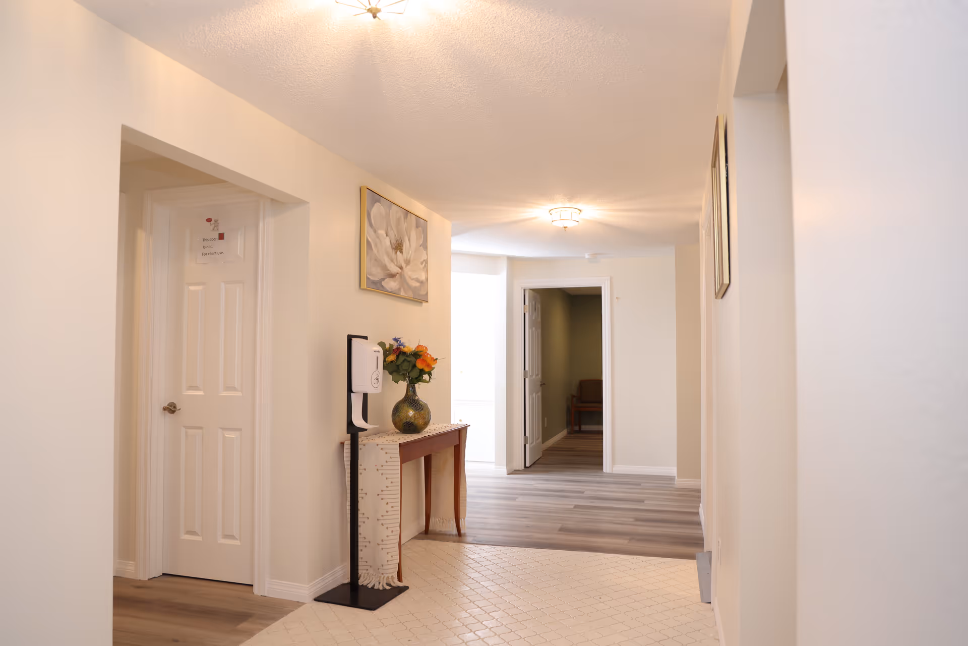Bright interior hallway of a senior living home with a console table, flowers, and wall art.