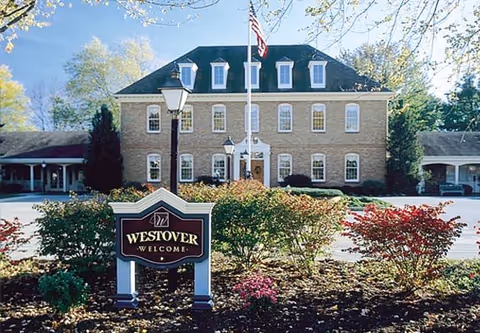 Front view of a brick retirement community building with a welcome sign and landscaping.