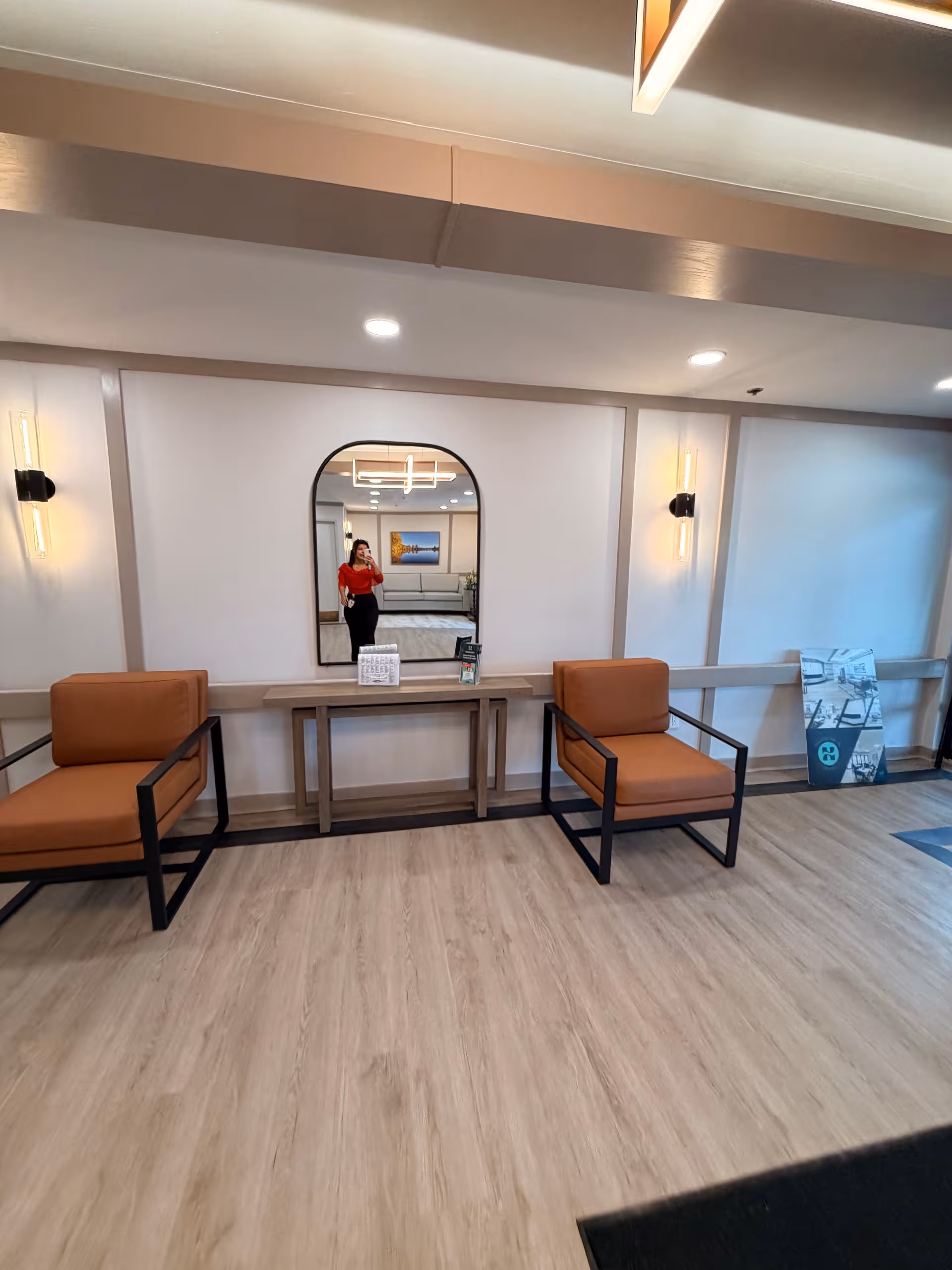 Modern lobby area with orange chairs, a console table, and a large mirror.