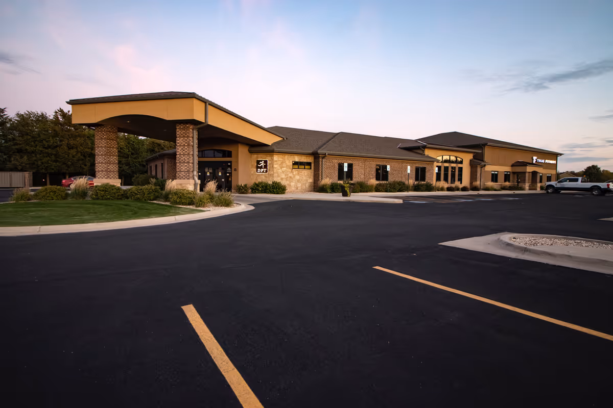 Exterior view of a single-story building with a covered entrance and expansive parking lot.