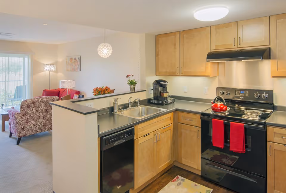 Open-concept kitchen with light wood cabinets, stainless appliances, and a view into the living area.