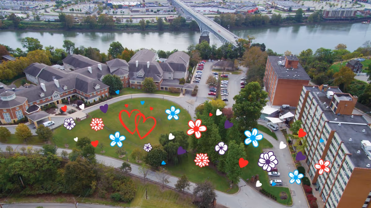 Aerial view of a senior living campus with brick buildings, green lawns, river, and bridge.