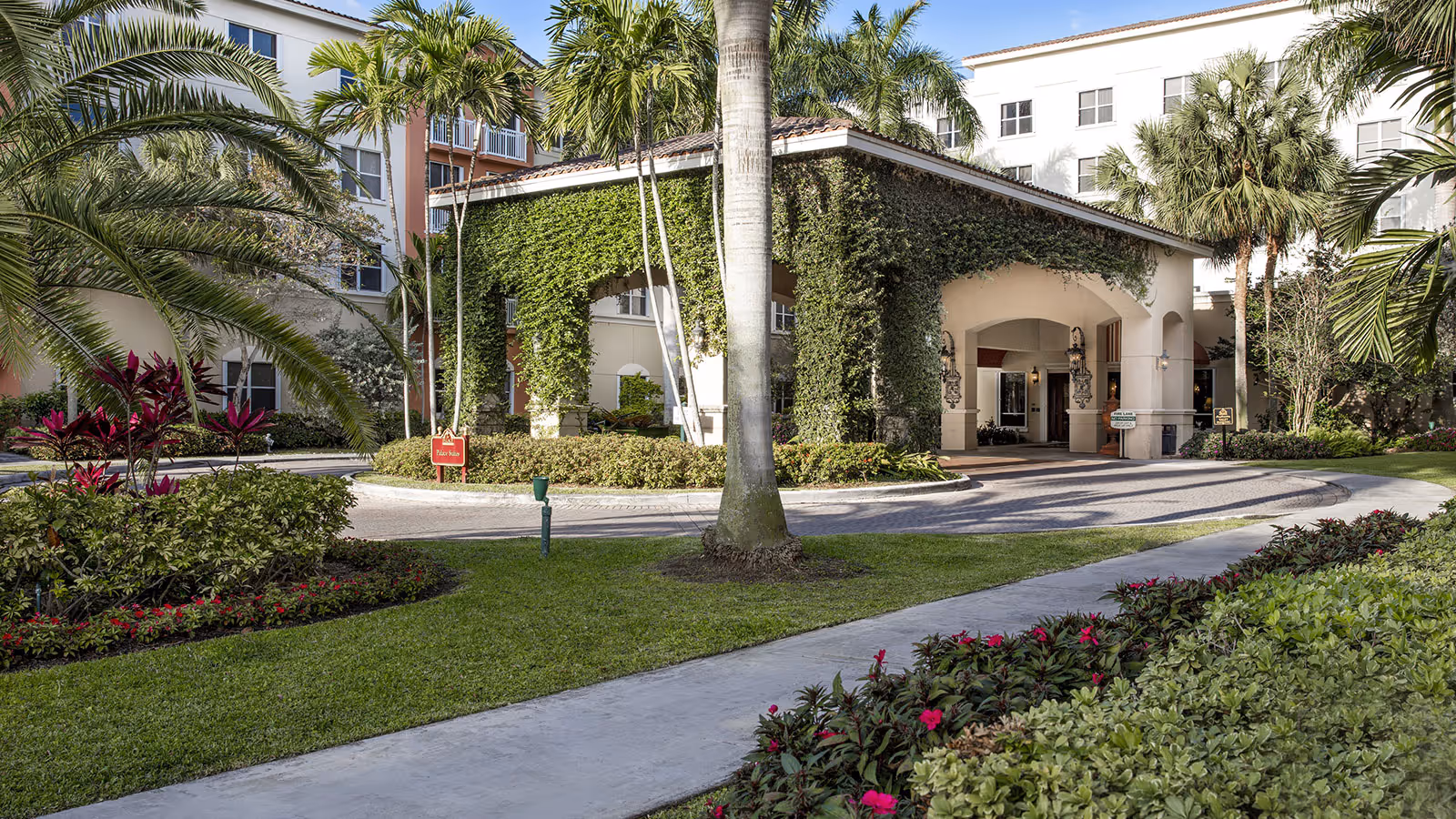 Exterior view of The Palace Suites with ivy-covered arches and palm trees.