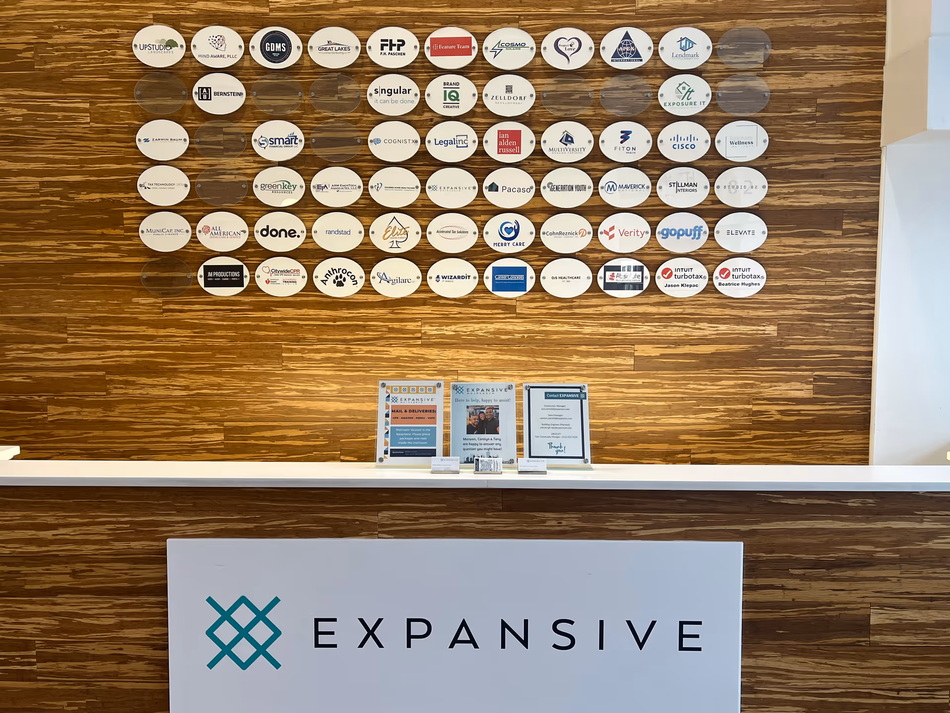 Reception area with a wooden wall displaying circular logos and a white counter.