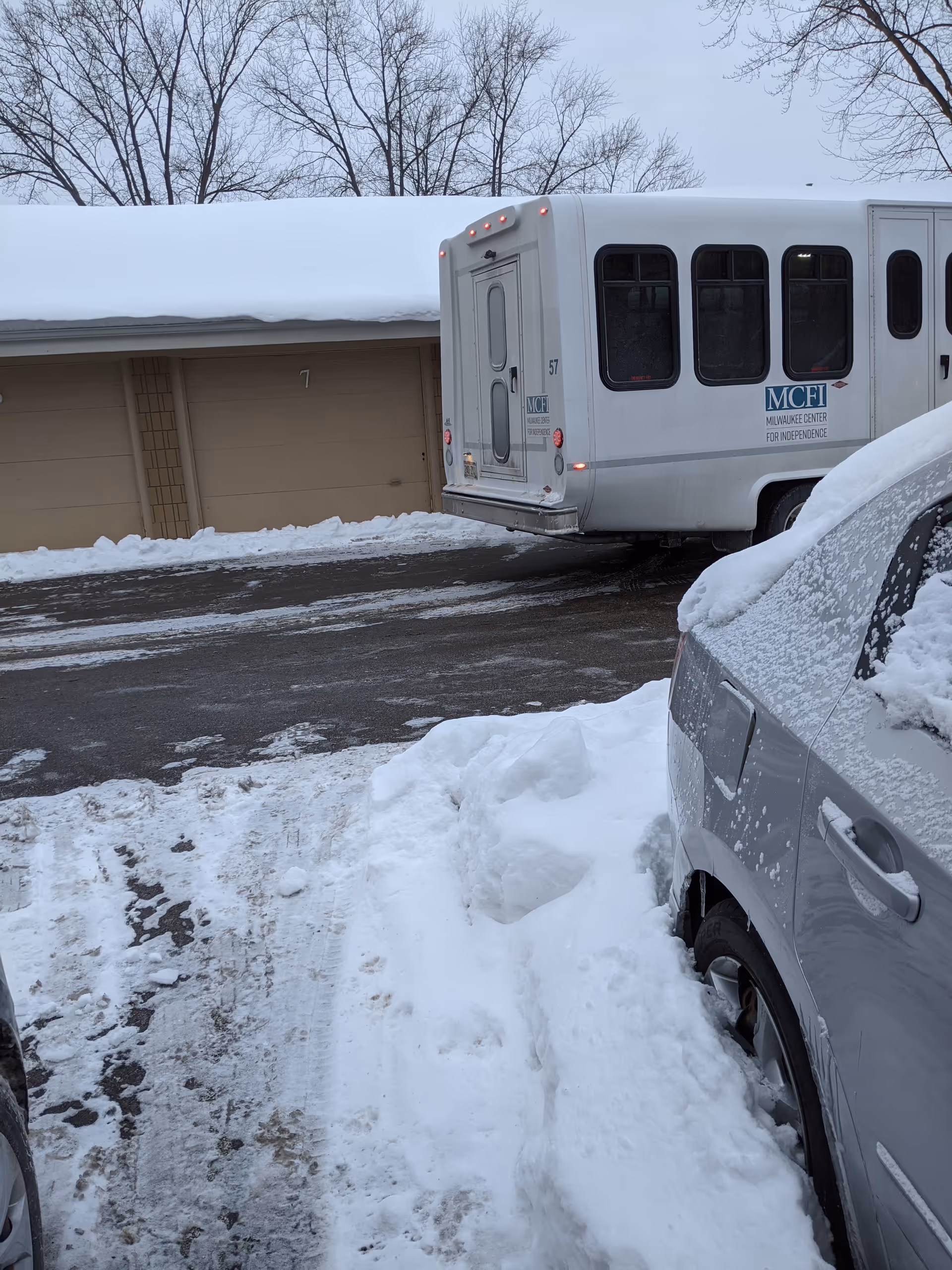 Snow-covered parking area beside a building with a parked shuttle bus.