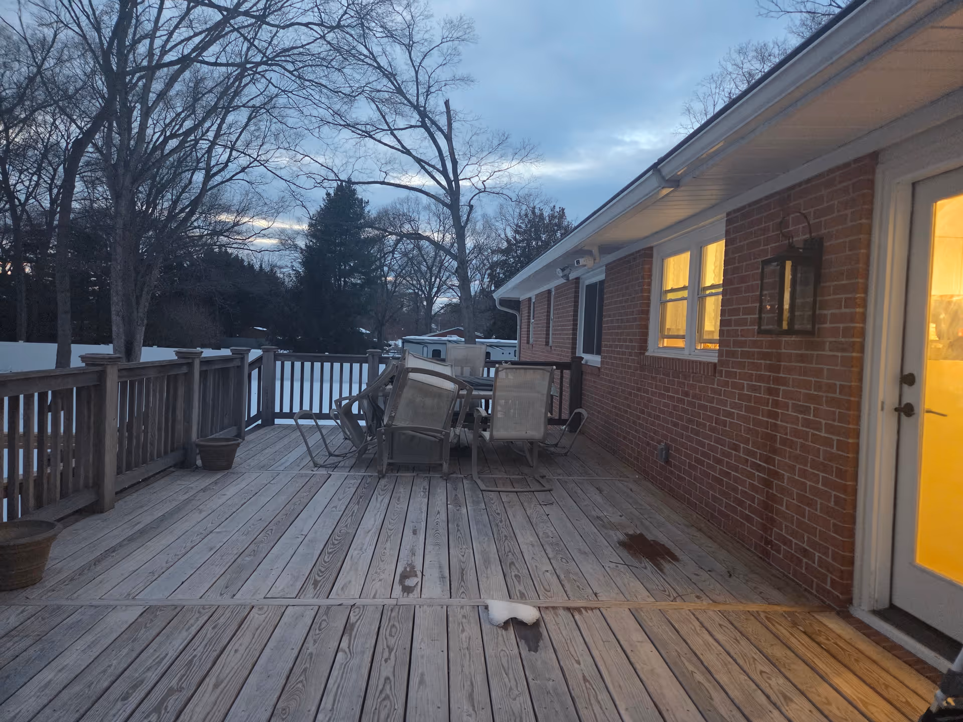 Outdoor wooden deck with chairs and a table attached to a brick building at dusk.