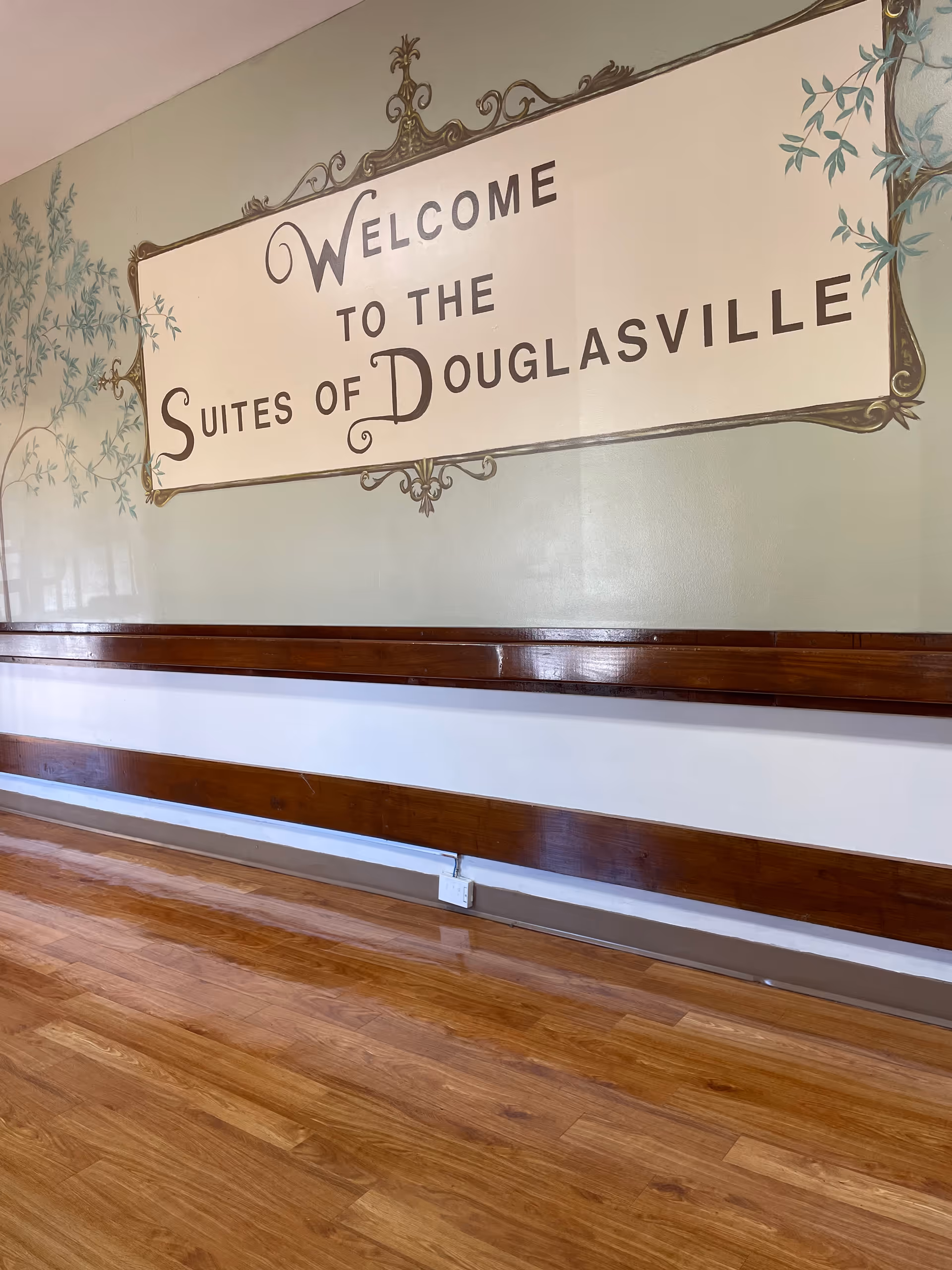 Lobby hallway with a large sign reading Welcome to the Suites of Douglasville and wooden benches.