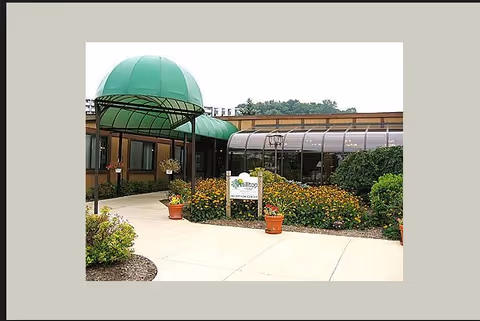 Entrance to Hilltop Village senior living with a green canopy, walkway, and flower planters.