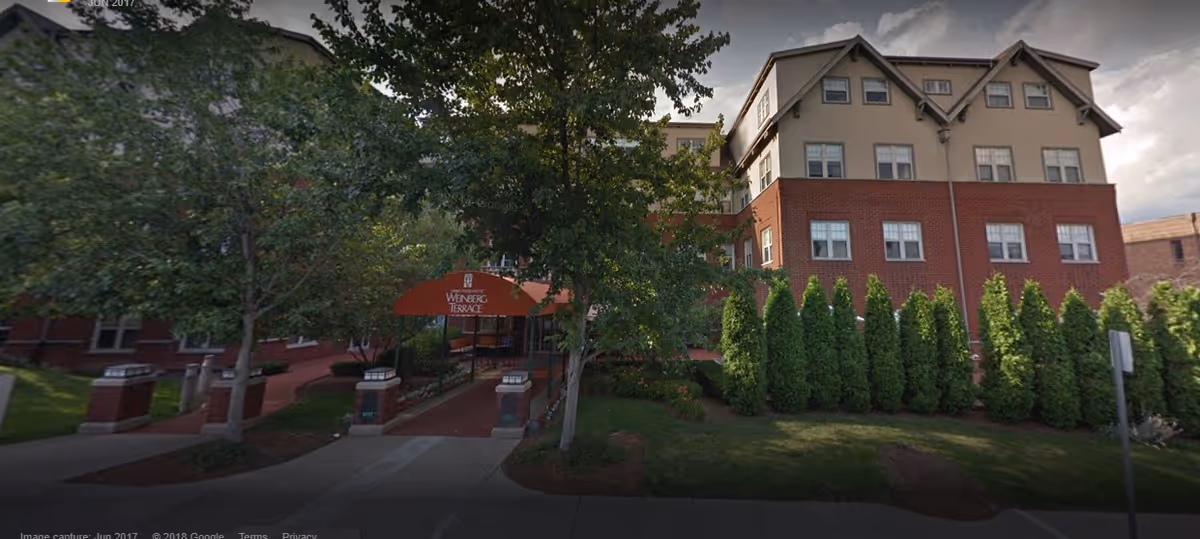 Front exterior of a multi-story brick and stucco senior living building with a covered entrance canopy reading "Weinberg Terrace".