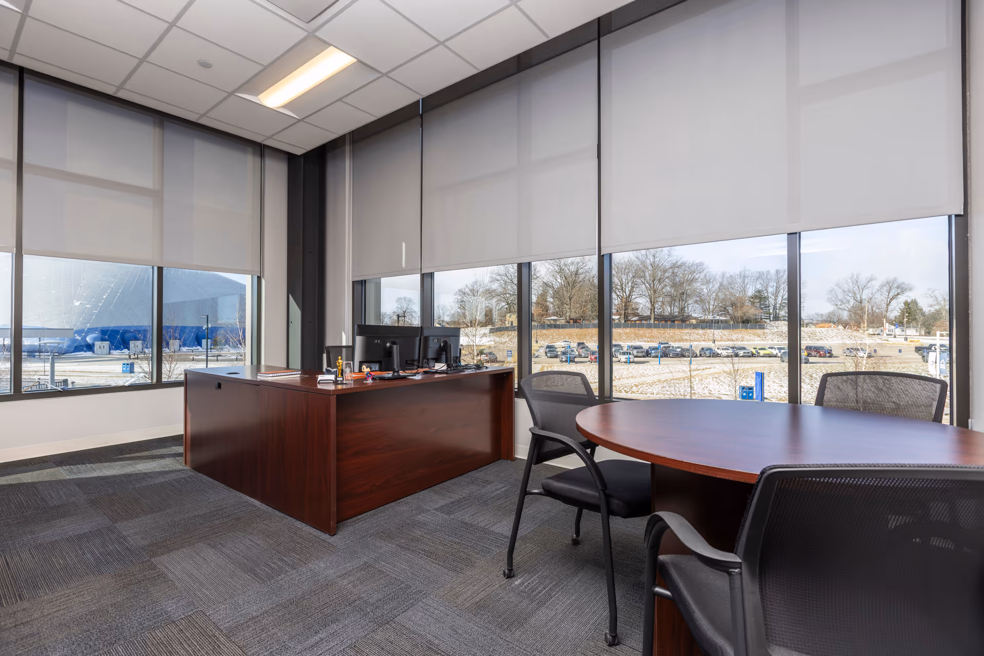 Modern office space with wooden desk, computer, round table, and large windows.