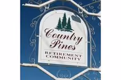 Decorative hanging sign reads Country Pines Retirement Community against a blue sky.