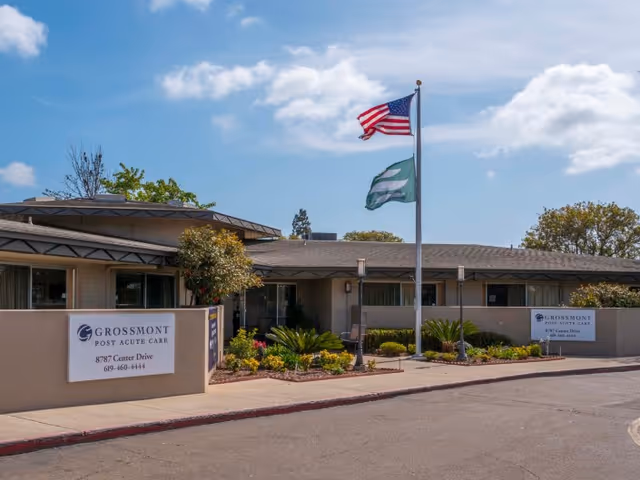 Front exterior of Grossmont Post Acute Care building with flags, signage, and landscaped entrance.