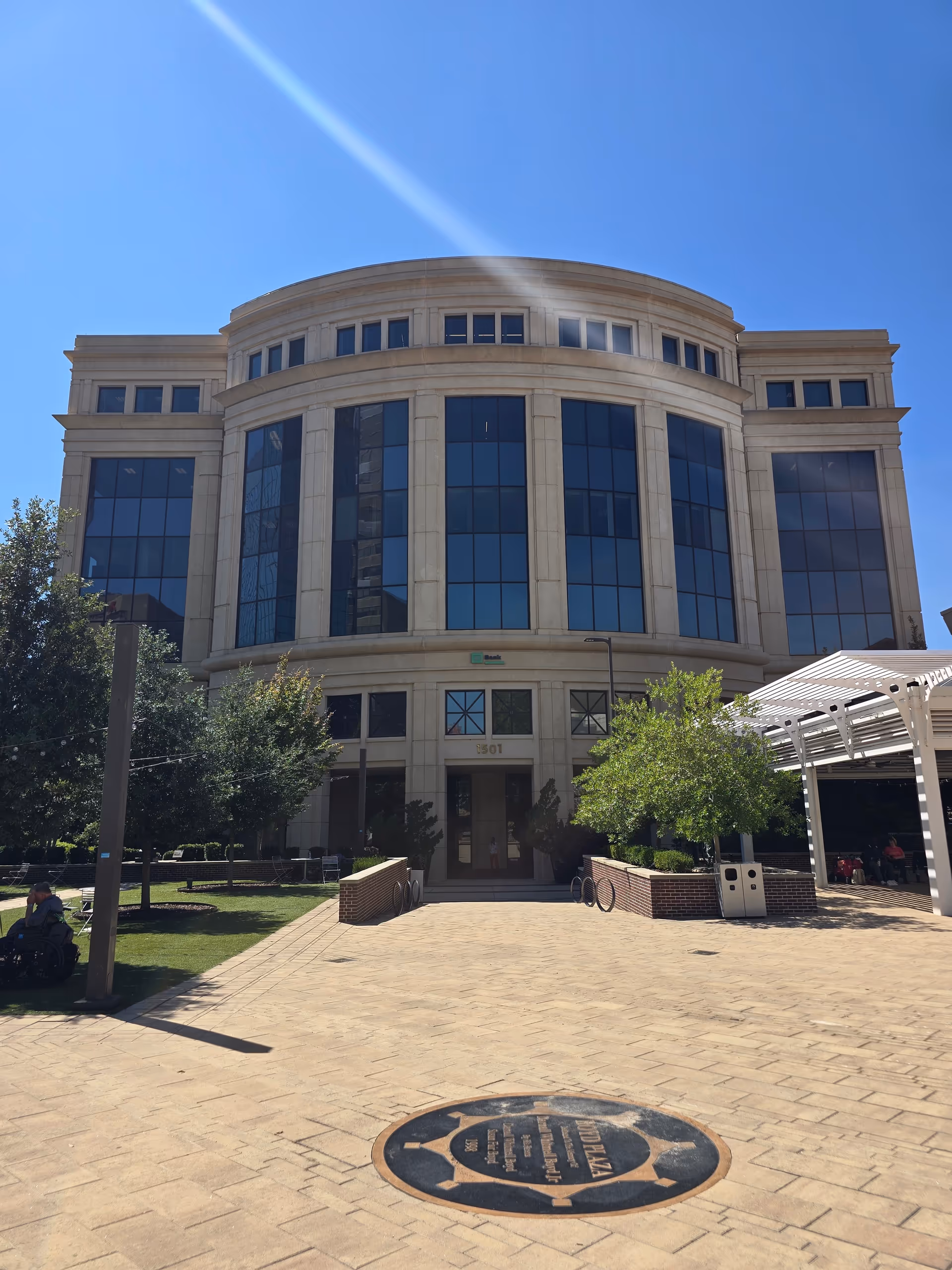 Large, modern stone building with curved glass windows and a paved plaza.