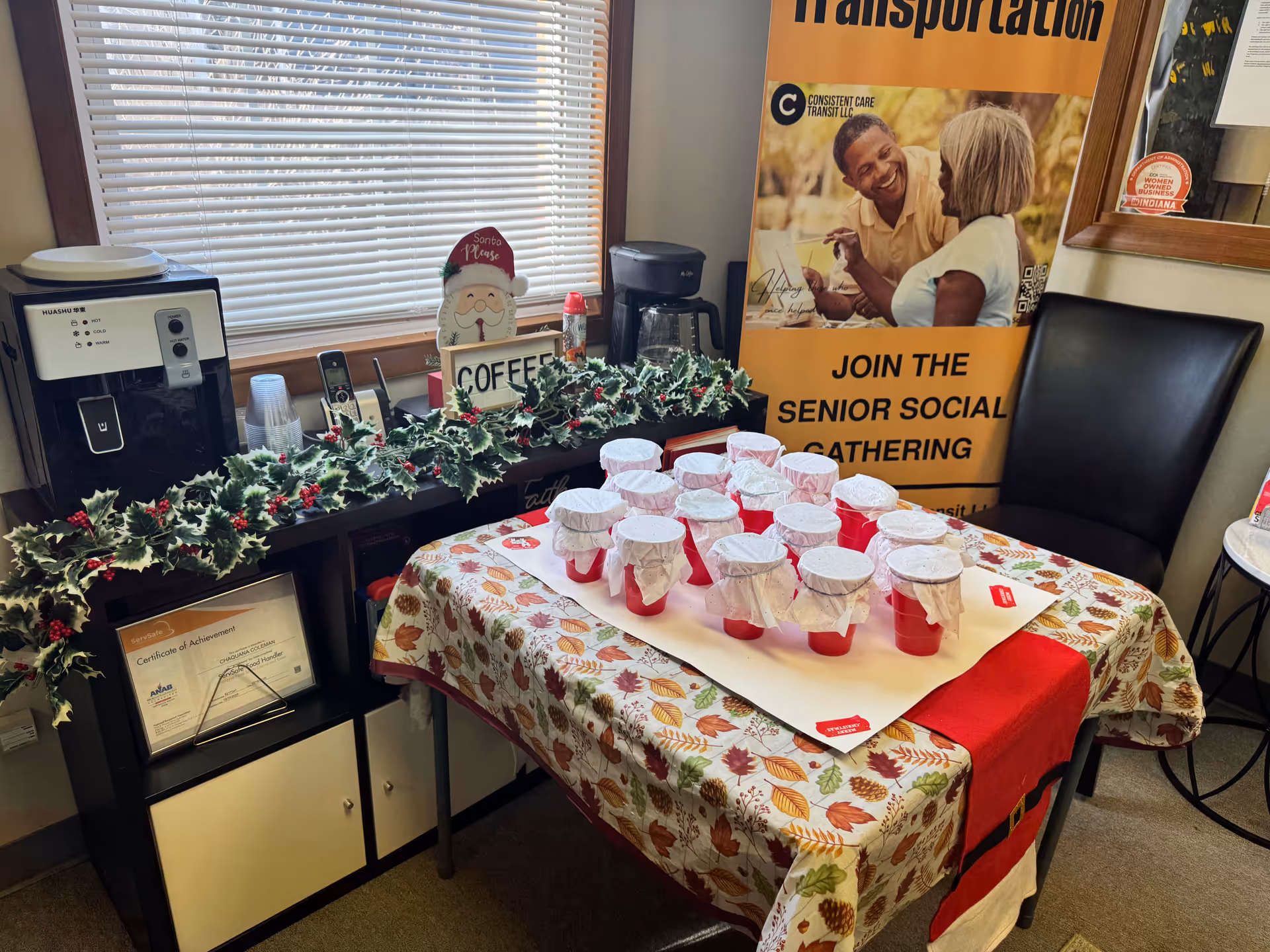 Indoor coffee station with cups on a leaf-patterned table and garland; banner in background.