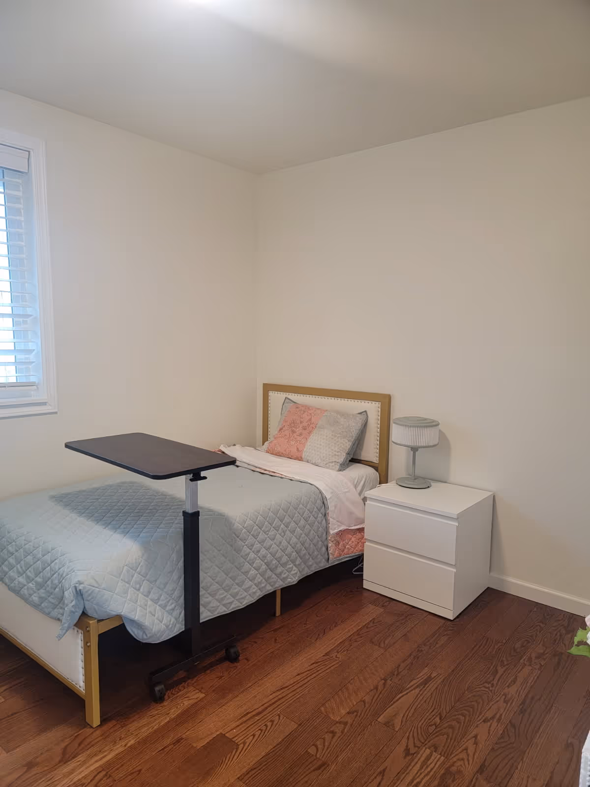 Small bedroom with single bed, nightstand, lamp, and wooden floor.